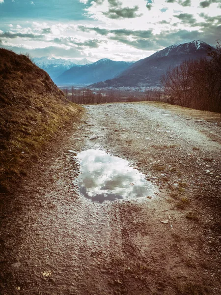 以高山为背景的崎岖道路 以云反射的水池 免版税图库照片