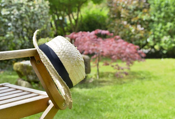 Słomkowy kapelusz na krześle w ogrodzie — Zdjęcie stockowe