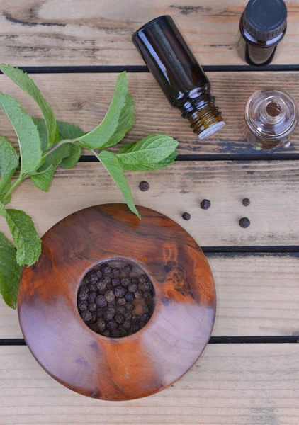 Essential oil from peppermint in bottle and fresh leaf of mint with pepper in bowl — Stock Photo, Image