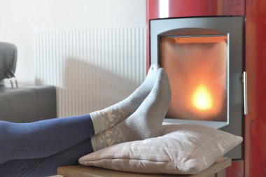 Çoraplı bir kadının ayaklarının manzarası bir odun sobasının önünde dinleniyor.