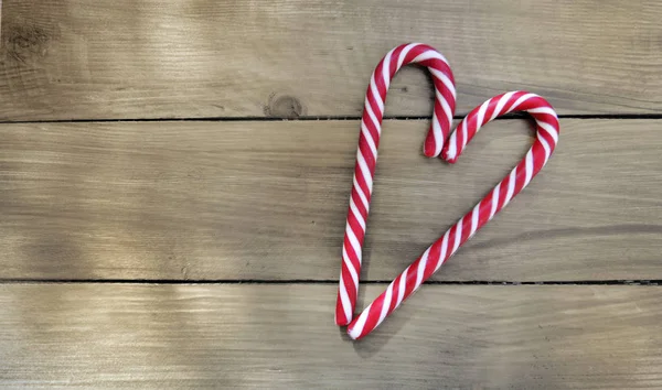 Candy canes forming a heart on wooden background — Stock Photo, Image