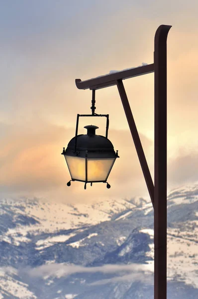 Lamp post in front of a beautiful sunset in snowy mountain — Stock Photo, Image
