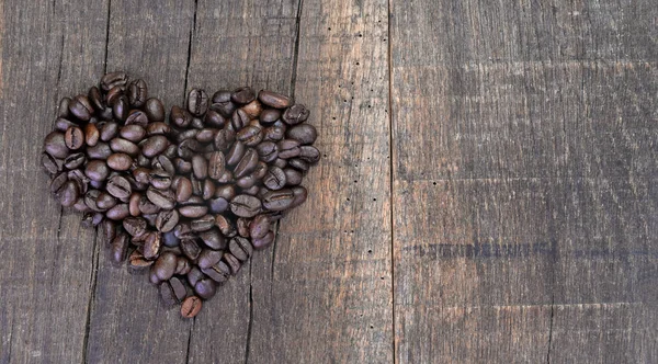 Fabricación en forma de corazón con granos de café dispuestos en una tabla rústica con espacio de copia a la derecha — Foto de Stock