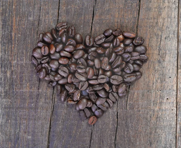 Fabricación en forma de corazón con granos de café dispuestos en una tabla rústica — Foto de Stock