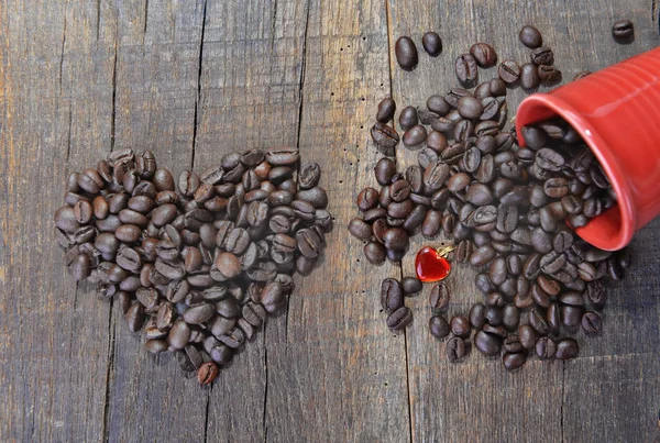 Corazón en forma de granos de café y una taza roja derramada con un concepto de joya en forma de corazón — Foto de Stock