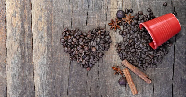 Corazón en forma de granos de café y rojo taza roja dispersa con especias en una tabla rústica — Foto de Stock