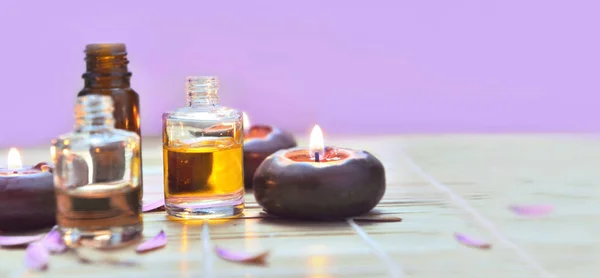 Garrafas de óleo com luz de velas em uma mesa no fundo rosa — Fotografia de Stock