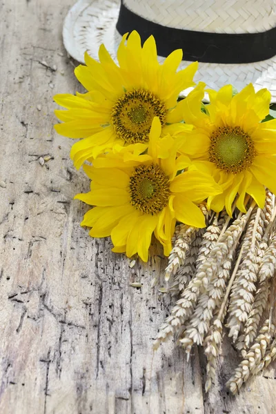 Bouquet of sunflowers and corn of wheat with a hat on a plank — Stock Photo, Image