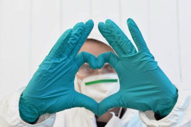 Koruyucu ekipman takan genç adam eldivenli elleriyle bir kalp oluşturuyor. 