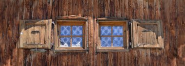 Eski bir dağ evinin ahşap cephesinde iki küçük pencereye yakın. 