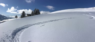 Mavi gökyüzünün altındaki taze karlı dağda kayak izleri.