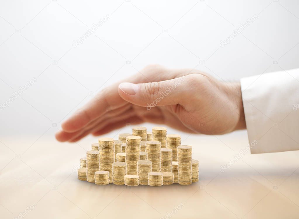 Stack of golden coins covered by hand. Savings protection concept 