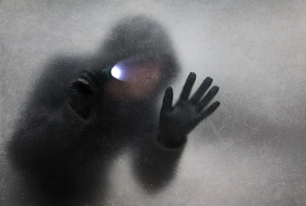 Ladrón con linterna detrás de un cristal rayado polvoriento — Foto de Stock
