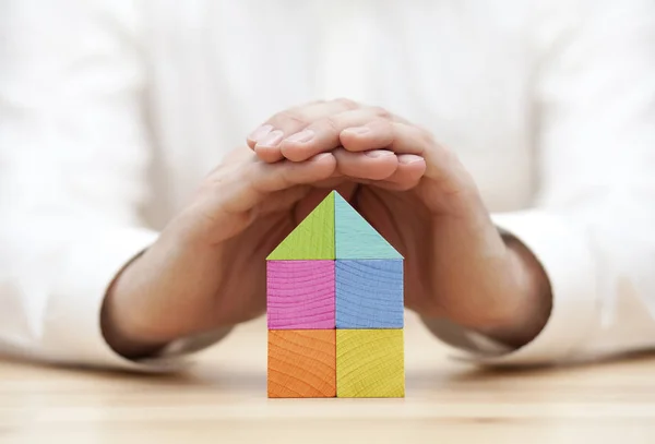 Kleurrijke houten blok huis beschermd door handen — Stockfoto