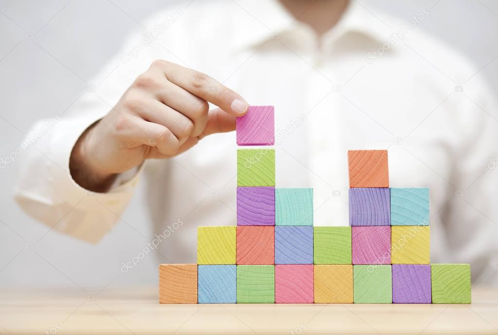 Man's hand stacking colorful wooden blocks. Business development concept 
