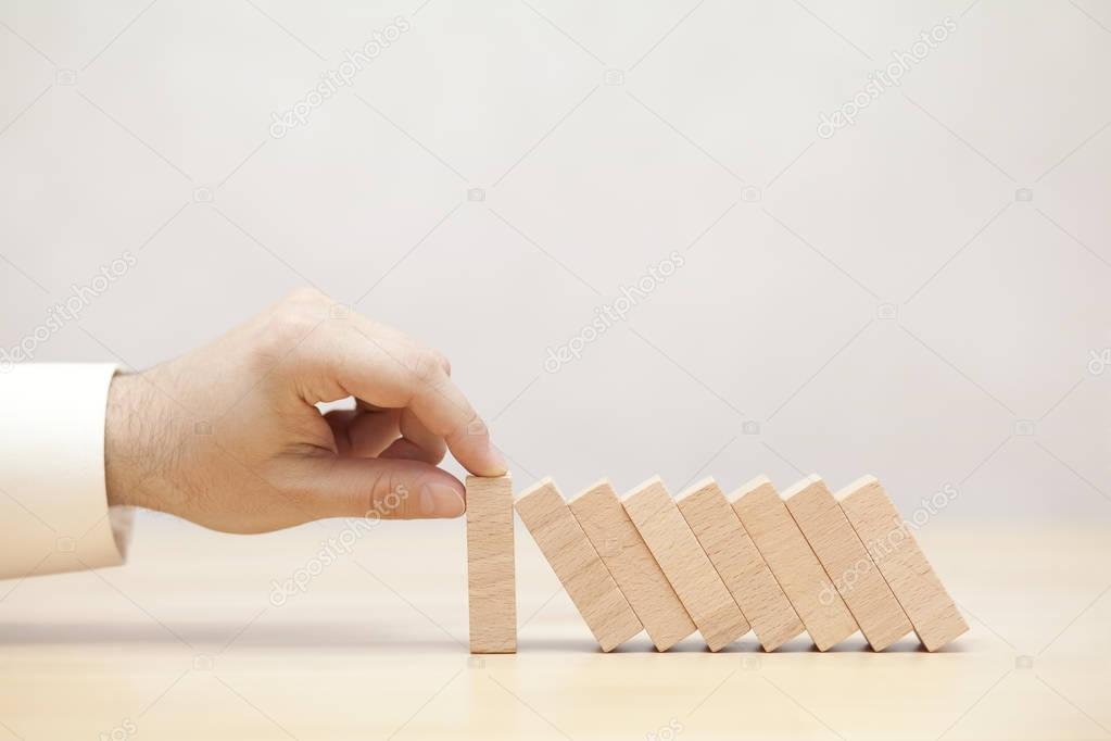 Man's hand stopping the domino effect. Concept image for business strategy and crisis solution. 