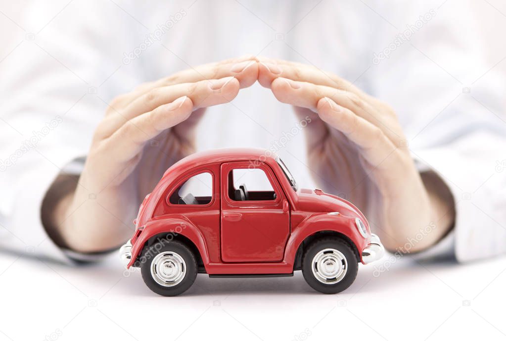 Car insurance concept. Red toy car covered by hands