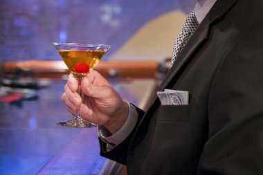 Barda oturan adam bir martini bir kiraz ile içinde tutarak, güzel koyu takım elbise ve kravat