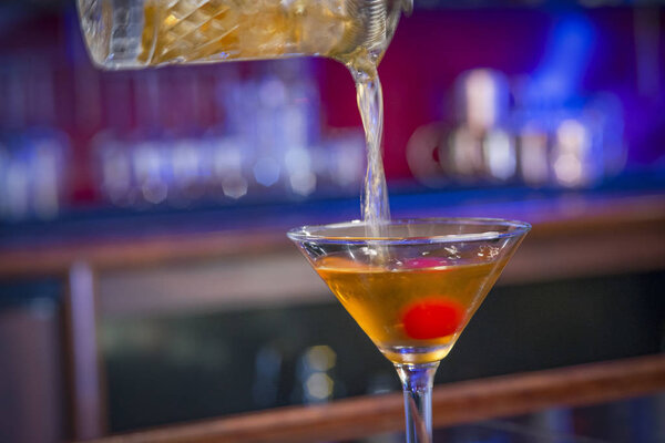 Close up of a drink being poured into a martini glass with a cherry, some motion blur