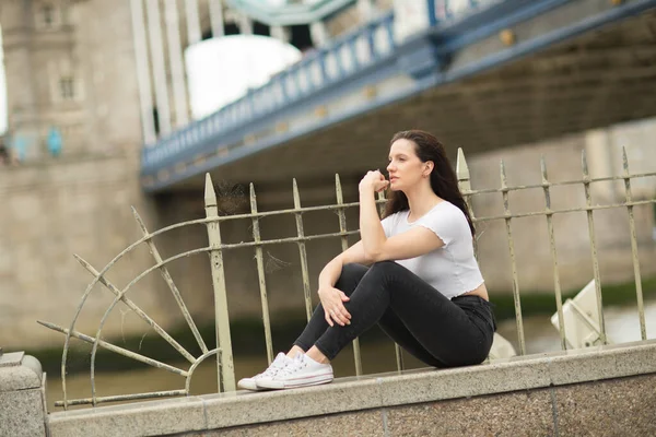 Genç Bir Kadın Köprünün Yanındaki Duvarda Oturuyor — Stok fotoğraf