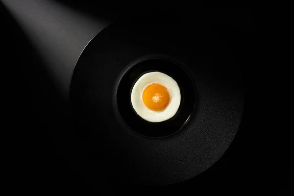 Stekt ägg i svart keramisk platta på svart bakgrund. Ovanifrån. — Stockfoto