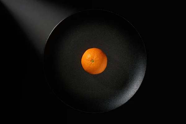 Tangerine i svart platta på svart bakgrund med stråle av ljus — Stockfoto