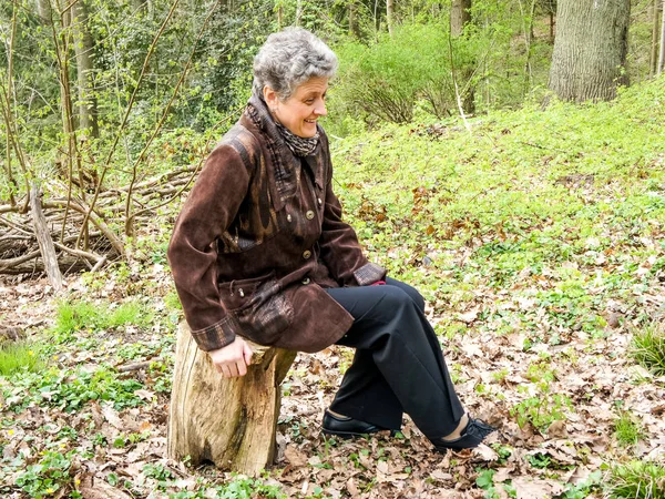 Volwassen vrouw rustend op een stomp in het park — Stockfoto