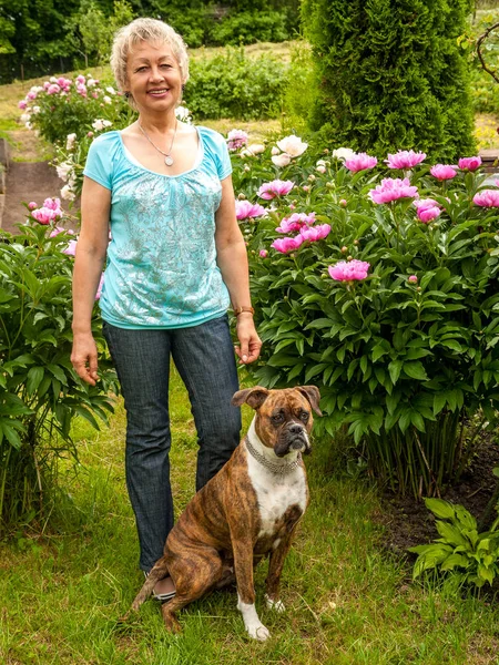 Gammal kvinna rastar sin hund i en park, ler och tittar på ca — Stockfoto