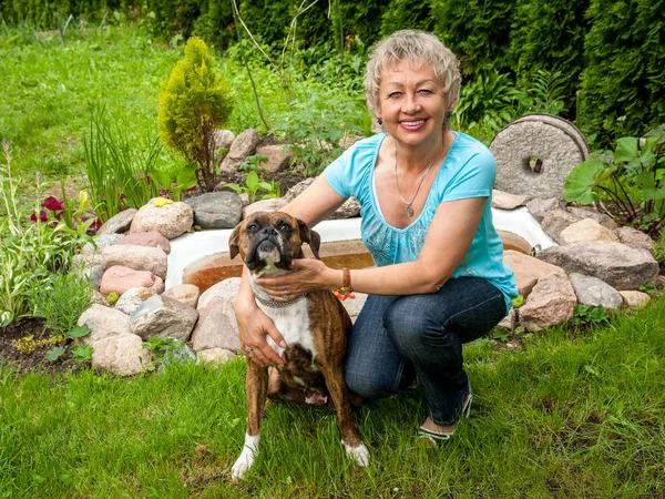 Mujer madura pasea a su perro en un parque, sonríe y mira a la ca —  Fotos de Stock