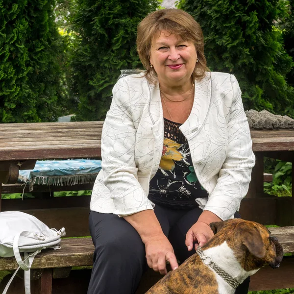 Reife Frau geht mit ihrem Hund in einem Park spazieren, lächelt und schaut die — Stockfoto