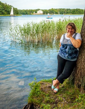 Olgun tombul kadın gölün kenarında dinleniyor.