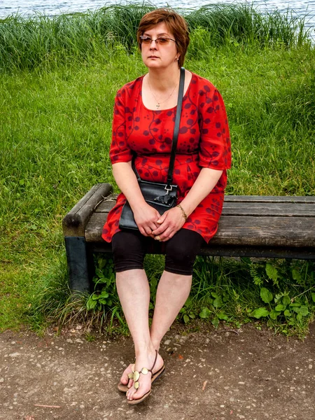 Зріла жінка в червоній сукні відпочиває на лавці — стокове фото