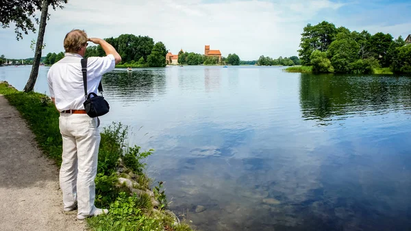 A Mature man looks at an ancient castle on an island. Trakai cas — Stock Photo, Image