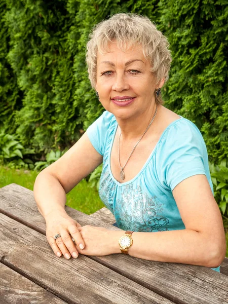 Starší žena sedící u dřevěného stolu a usmívající se — Stock fotografie