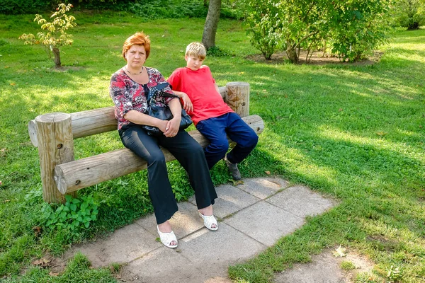 Mor og søn går i byparken. Sidder på en bænk af l - Stock-foto