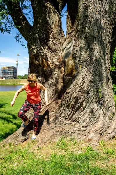 Mature woman in red resting near a huge tree by the river — Stock Photo, Image