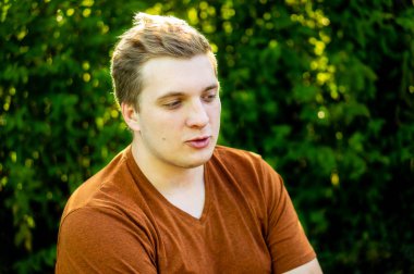 Genç bir adam şehir parkında yürüyor, bankta oturuyor. 