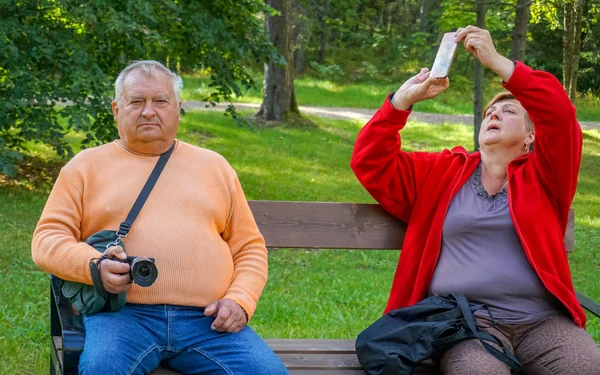 Зрелые туристы ходят и фотографируют в парке у воды — стоковое фото