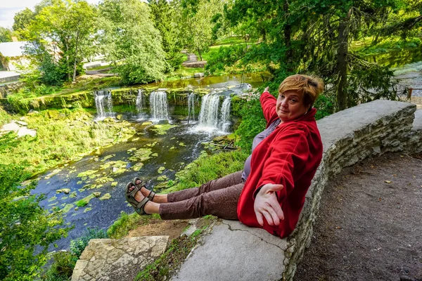 Зрелая пухлая женщина в красном, отдыхающая у водопада — стоковое фото