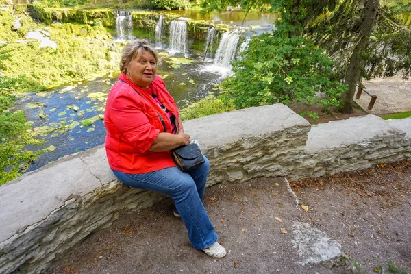 Gammal fyllig kvinna i rött vilar vid vattenfallet — Stockfoto