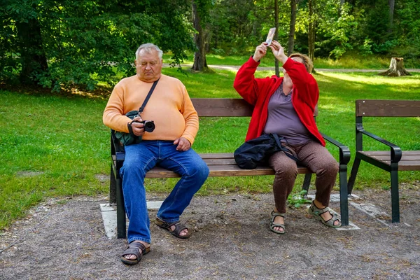 Семейная пожилая пара отдыхает, сидит на скамейке и фотографируется — стоковое фото