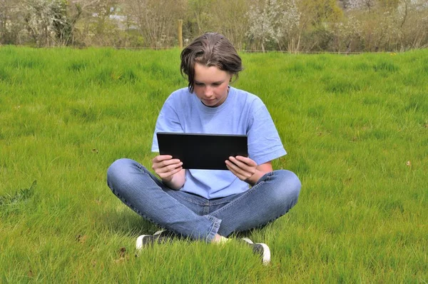Девушка сидит на газоне и с помощью цифрового планшета — стоковое фото