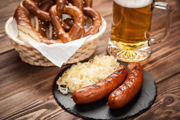 Pretzels, bratwurst and sauerkraut on wooden table — Stock Photo, Image