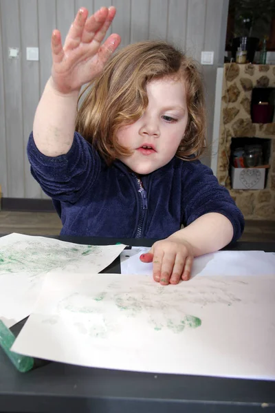 little blonde girl painting with her hands and fingers on paper