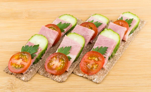 Three crisp bread with bacon, cucumbers and tomatoes on table