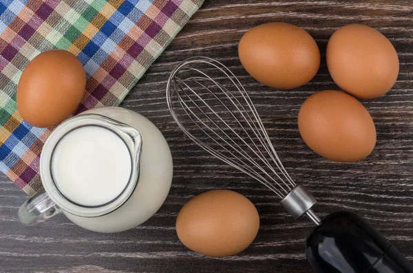 Eggs, milk jug and whisk on dark table