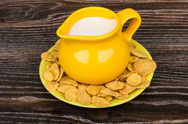 Yellow jug milk in saucer with corn flakes on table