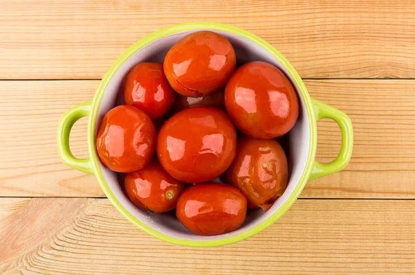 Green glass bowl with red pickled tomatoes on wooden table