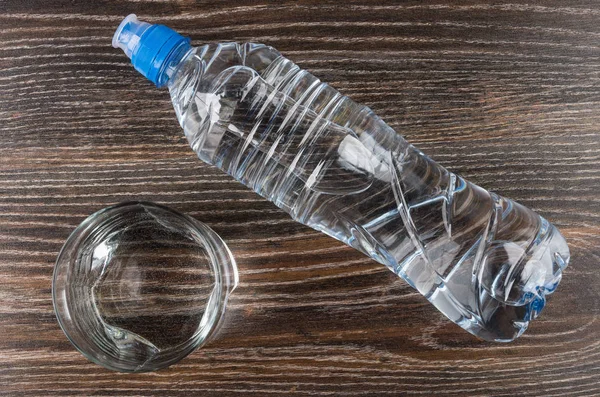 Glass water and lying plastic bottle on wooden table