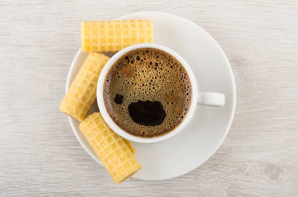 Coffee cup and wafer rolls on saucer on wooden table